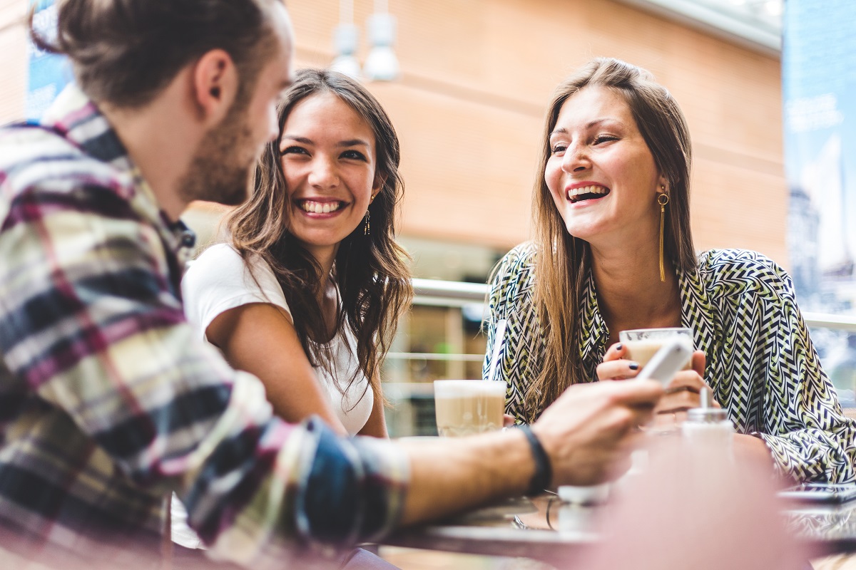 Multiracial group of friends having a coffee together. Two women and a man at cafe, talking, laughing and enjoying their time. Lifestyle and friendship concepts with real people models.