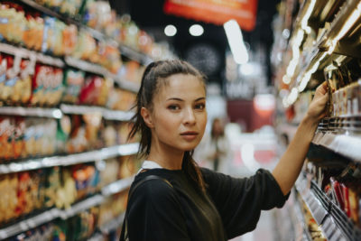 Woman reaching for a product in a supermarket. Is it vegan? Our vegan food labelling guide will help you.