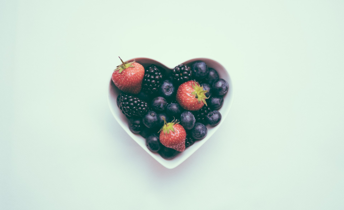 A heart-shaped bowl filled with strawberries and blueberries. High blood pressure is a global health condition.