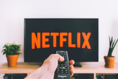 Unidentified person pointing remote at TV screen and watching Netflix