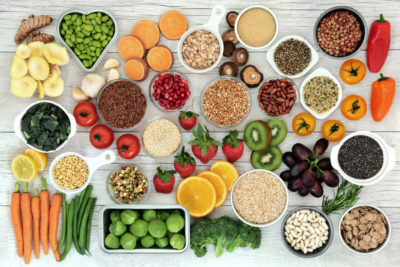 A flatlay of vegan superfoods - with fruit, vegetables, grains, cereals, pulses, seeds, herbs and spice. Foods high in fiber, anthocyanins, antioxidants, smart carbs, minerals and vitamins.