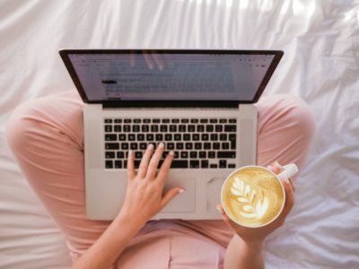 Woman holding coffee and typing on laptop