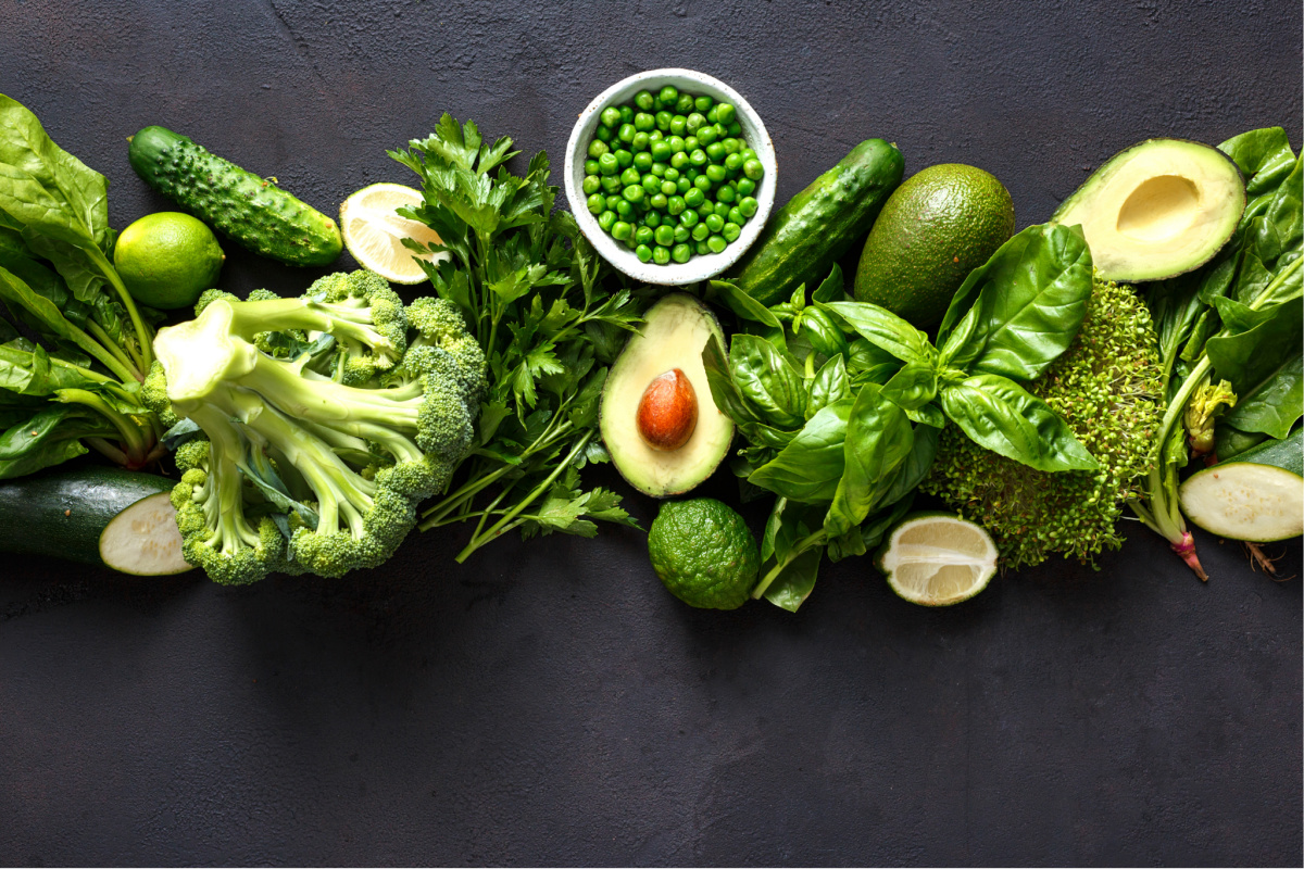 Raw healthy food clean eating vegetables: cucumber, alfalfa, zucchini, spinach, basil, green peas, dill, parsley, avocado, broccoli, lime on dark stone background, top view