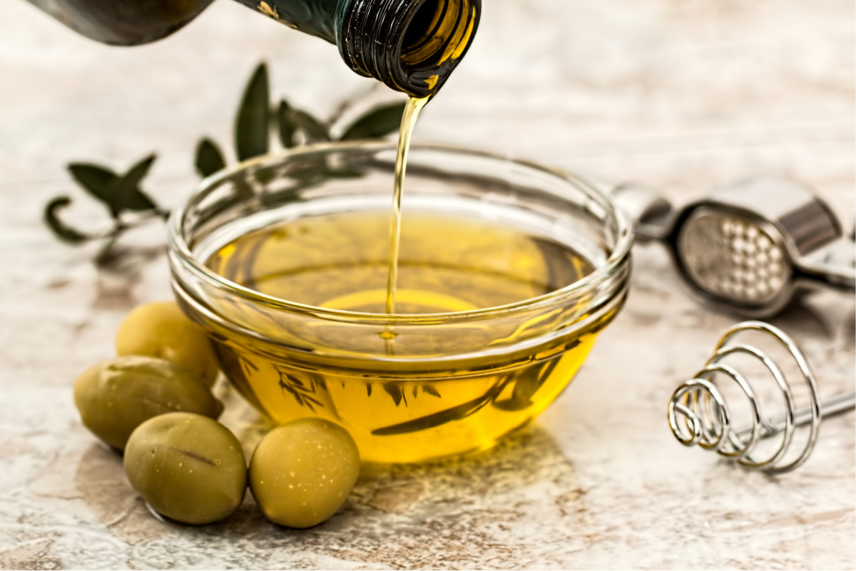 Unidentified person pouring olive oil into a glass dish - oil is another vegan supermarket essential
