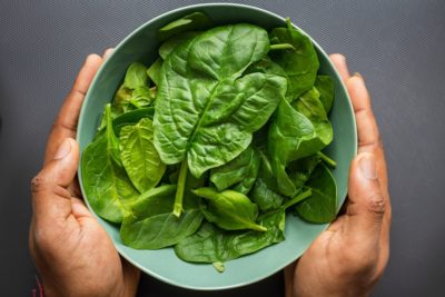 Unidentified person holding a bowl of raw spinach - a key source of iron for vegans