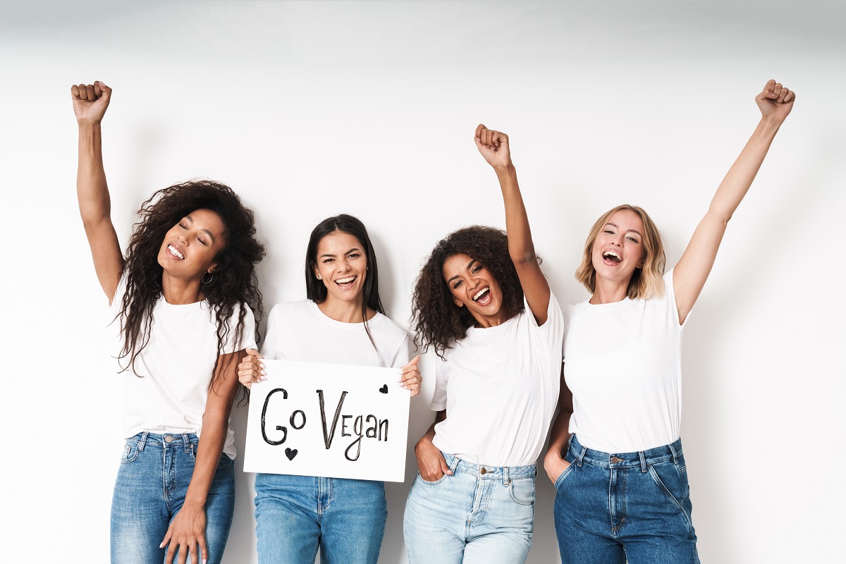 Image of a happy cheery emotional young women multiracial friends posing isolated over white wall background holding blank with motivation vegan text.