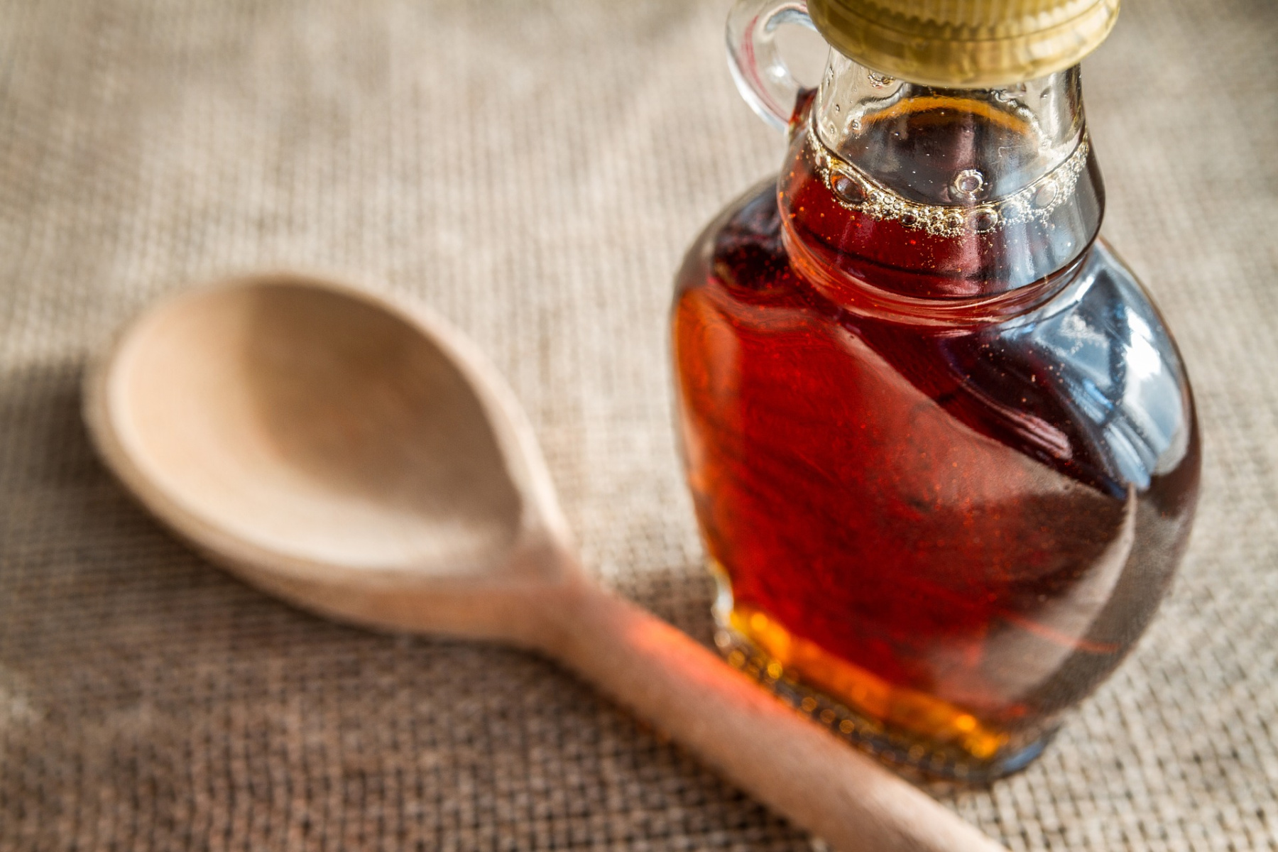 A glass bottle of maple syrup and a wooden spoon