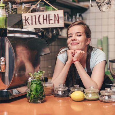 A young Caucasian woman leaning on a cafe counter smiling