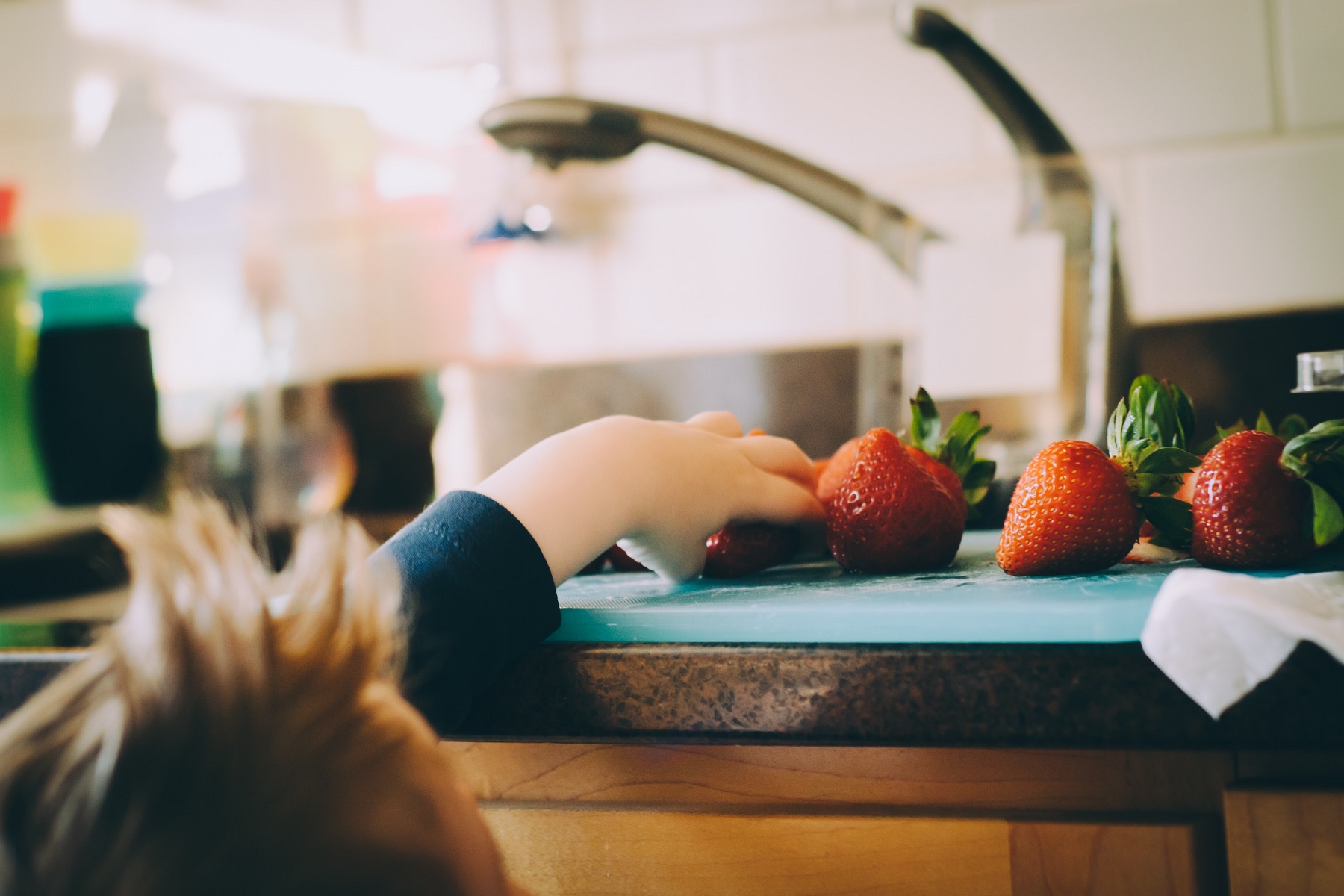 Child reaching up onto the worktop for a piece of fruit. In this guide we discuss how to cook with vegan children.