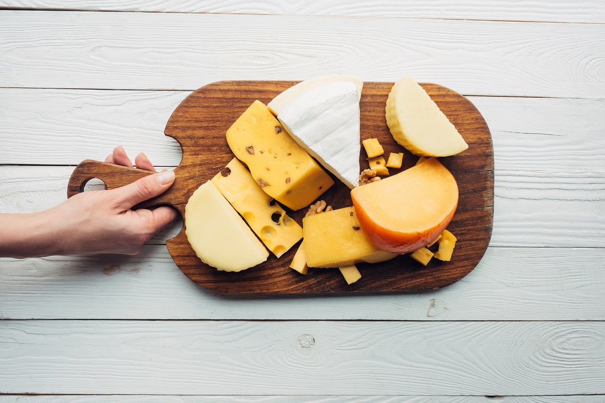 hand and assorted cheese on wooden board