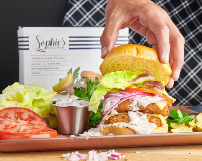 Fish burger on a bun with tomato, lettuce, and tartar sauce, in front of a package from Sophie's Kitchen