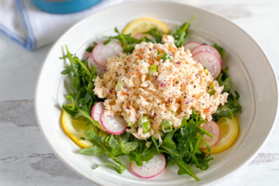 Bowl of vegan shrimp salad arranged on a plate with arugula, lemon, and radish