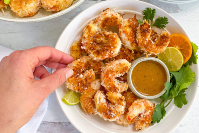 A hand reaching for a plate of vegan coconut shrimp