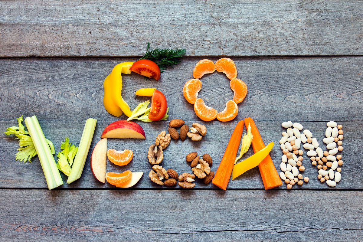 Words "Go Vegan" written with vegetables, fruits, nuts and legumes on rustic wooden background, concept - organic ingredients for healthy vegan food and lifestyle