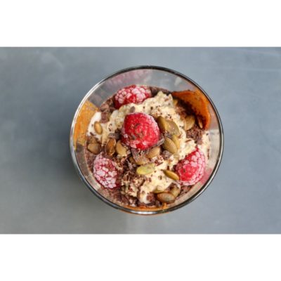 a clear glass bowl is filled with oats, chocolate, peanut butter, and frozen raspberries