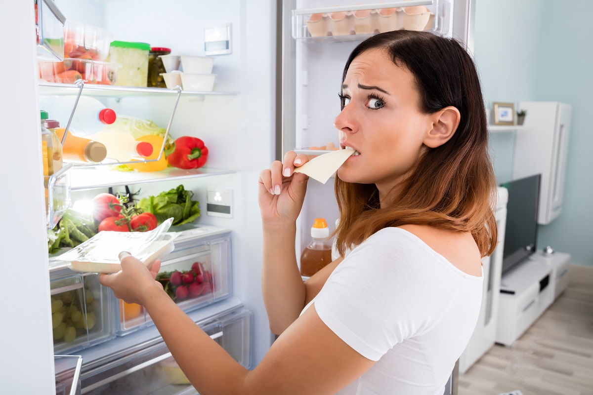 Woman Eating Cheese In Front Of Refrigerator