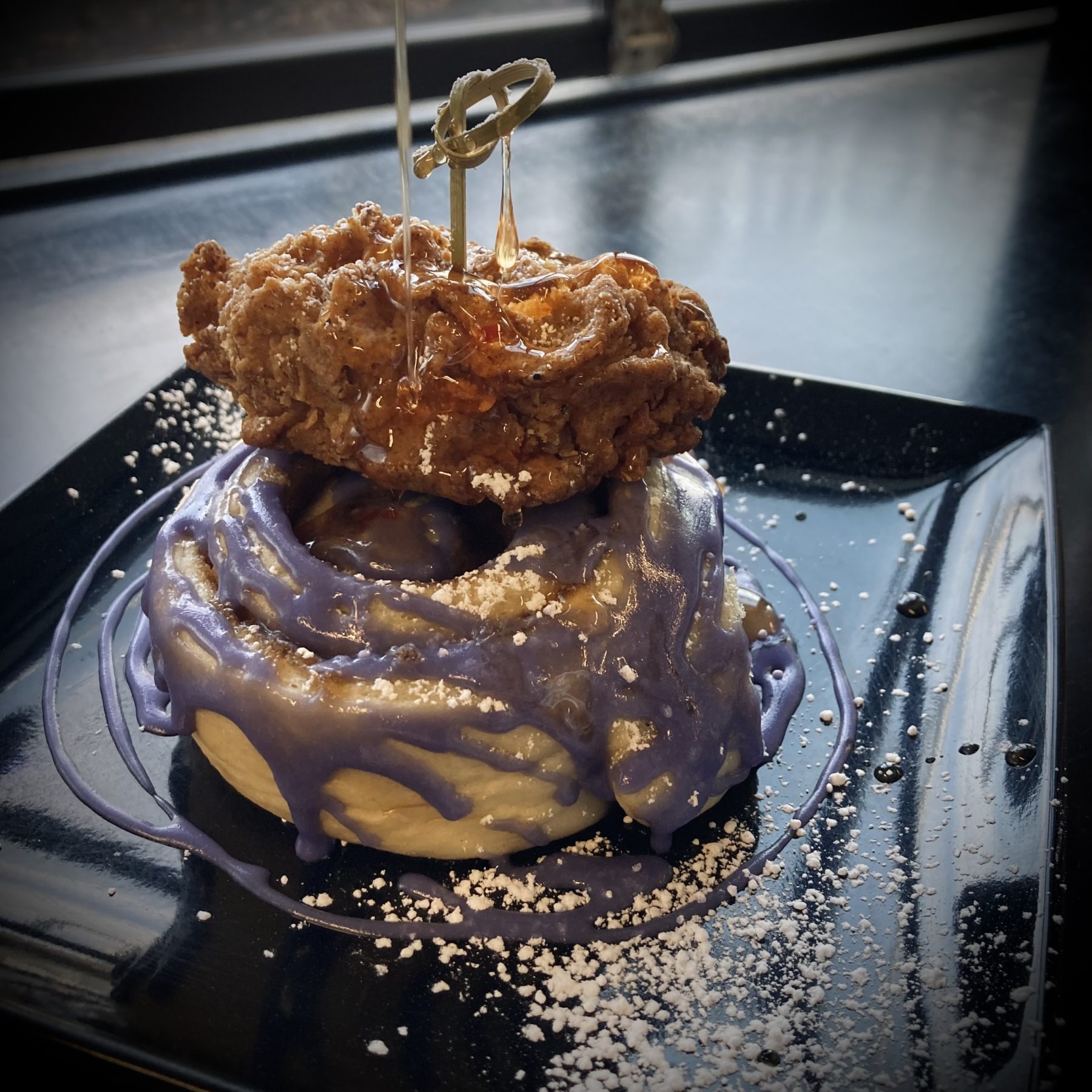 Hail Snail's cinnamon roll topped with purple syrup, vegan chicken, and spicy vegan honey