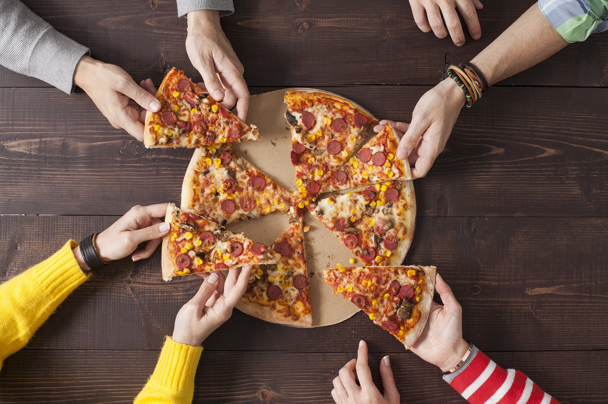 Top view shot of a group of people's hands each grabbing a slice of pizza