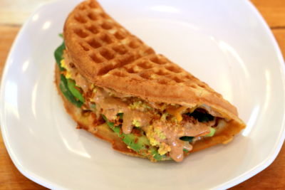 Tiabi's wafflewich shows a waffle folded in half and stuffed with tofu scramble, avocado, vegan bacon, and spicy aioli
