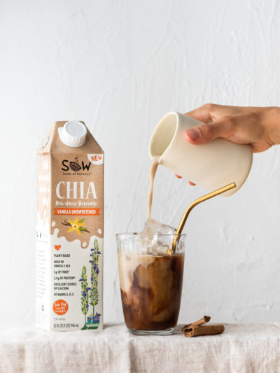 Seeds of Wellness chia non-dairy milk is poured into a crisp glass of iced coffee in a clear glass with a gold metal straw