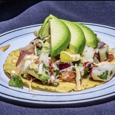 A crispy tostada is topped with hearts of palm ceviche and three giant fresh slices of avocado