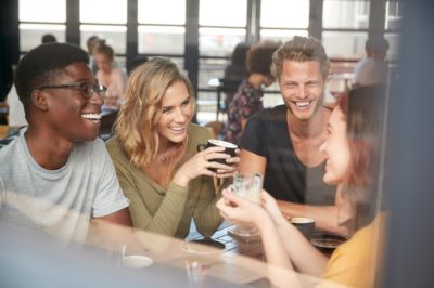 Group Of Friends Sitting At Table In Busy Coffee Shop Talking