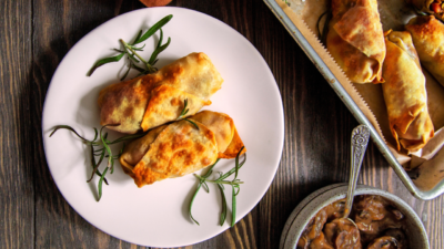 Two crispy Thanksgiving spring rolls sit on a white plate garnished with rosemary