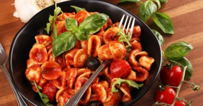 a black bowl of delicious pasta with tomato sauce and olives garnished with fresh basil