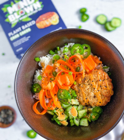 A rice bowl featuring Mind Blown Crab Cakes garnished with fresh cucumber and carrot