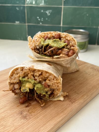 a burrito stuffed with rice, mushrooms, and avocado is cut in half and stacked