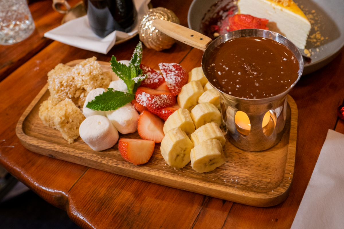 A platter features fresh fruit, marshmallows, and vegan rice krispies next to a chocolate fondue over a tea light candle