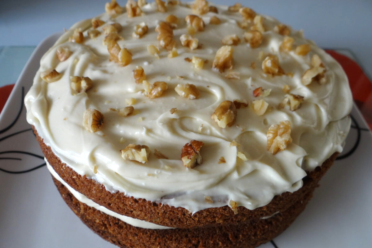 A moist carrot cake topped with vegan cream cheese frosting and walnuts