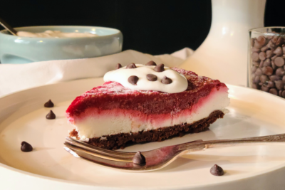A slice of raspberry cream pie features a chocolate crust followed by a layer of cream, topped with a raspberry puree