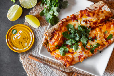 Vegan chicken enchiladas on a table with limes and cilantro