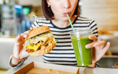 A young woman drinks green smoothies and eats a burger in a vegan fast food restaurant