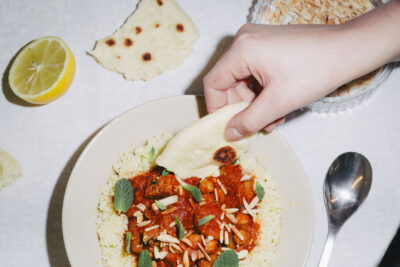 Image of a hand dipping flatbread into a bowl of chickpea tagine served over rice.