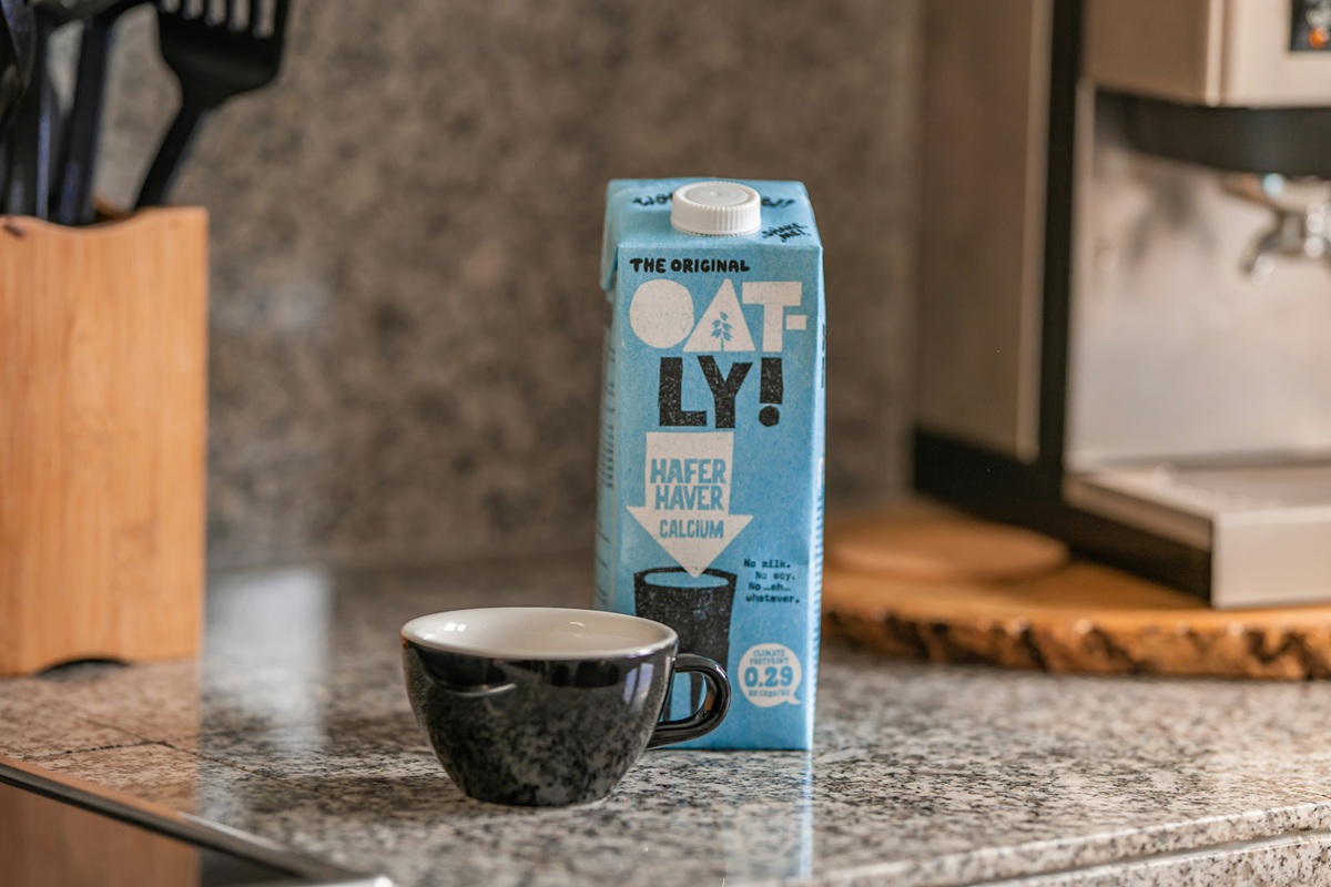 A carton of Oatly plant milk and cup of coffee on a kitchen countertop